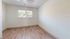 Bright bedroom with hardwood flooring and a window view, featuring modern simplicity.