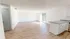 Bright open living space with wood flooring, large windows, and adjacent kitchen area.
