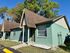 Charming green duplex with sloped roofs and inviting front porch, surrounded by lush trees under a clear blue sky.