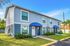 Charming double-story apartment with blue accents, featuring modern windows and lush landscaping under a clear sky.