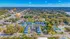 Breathtaking aerial view of a serene suburban neighborhood, featuring a cluster of modern blue-roofed apartments and a central swimming pool, surrounded by lush greenery and vast landscapes under clear blue skies.
