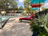 Inviting poolside area featuring vibrant red and teal lounge chairs under colorful umbrellas, surrounded by lush greenery and clear blue skies.