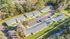 Charming aerial view of a well-maintained apartment complex with spacious parking and lush green surroundings, nestled beside a serene wooded area.