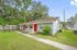Charming duplex with vibrant red doors, surrounded by lush greenery and mature trees, offering a cozy and inviting exterior.