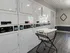 Modern apartment laundry room featuring a sleek row of white washers and dryers with a stylish laundry cart on polished wood flooring.