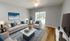 Elegant living room with plush beige sofas, blue accents, a modern marble coffee table, and natural light from large glass doors opening to greenery.