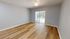 Bright, empty bedroom with sleek hardwood floors and a sliding glass door leading to a lush outdoor view.