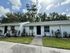 Charming single-story apartment with fresh white exterior, modern black doors, and lush landscaping under a clear blue sky.