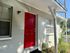 Inviting apartment entrance with a bold red door, surrounded by lush greenery and ample natural light.