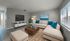 Modern living room featuring plush beige sectional sofa with vibrant teal cushions, chic wooden coffee table, wall-mounted TV, and large window for natural light.