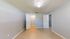 Bright empty room with light gray walls, tiled flooring, and a ceiling fan, featuring two white doors leading to a walk-in closet and adjacent room.