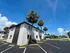 Charming apartment building with pristine white exterior and lush palm trees, offering ample parking and vibrant blue skies above.