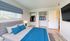 Bright and airy bedroom featuring a plush gray bed with blue accents, dual closets with contemporary wardrobe, and a wall-mounted flat-screen TV.