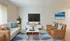 Inviting living room with stylish wicker furniture, elegant TV setup, and coastal artwork, perfect for relaxation and entertainment.