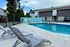 Inviting poolside area with modern lounge chairs and a serene blue swimming pool, surrounded by lush greenery and contemporary apartments.