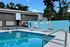 Inviting pool area with relaxing lounge chairs in a serene apartment complex setting, enhanced by lush greenery.