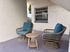 Charming patio corner featuring two stylish wicker chairs with teal cushions and a matching round table, perfect for relaxing.