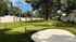 Charming outdoor view with a well-maintained putting green surrounded by lush greenery and quaint cottages under a clear blue sky.