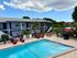Charming apartment complex featuring a picturesque pool area with red lounge chairs, umbrellas, and lush greenery backdrop.
