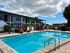 Inviting apartment complex with a sparkling pool, cozy red loungers, and a charming outdoor seating area under umbrellas.