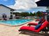 Inviting apartment complex pool area with bright red loungers and umbrellas under a clear blue sky.