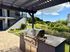 Charming outdoor area featuring a sleek stainless steel grill under a stylish pergola, surrounded by lush greenery and a cozy patio setting.