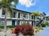 Inviting two-story apartment with lush landscaping and palm trees under a clear blue sky.