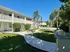 Charming two-story apartment complex with lush greenery, palm trees, and a modern outdoor BBQ area, perfect for relaxation.