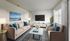 Chic modern living room with plush beige sofas, vibrant blue cushions, and a sleek marble coffee table. Elegant decor featuring stylish plants, artistic wall painting, and ample natural light.
