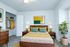 Inviting bedroom with a mid-century modern design, featuring a cozy bed with vibrant yellow and green accents, stylish wooden furniture, and an open closet space.
