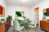 Chic dining area with a modern glass table, stylish green chairs, vibrant art, and sleek wooden cabinet, offering a cozy and inviting atmosphere.