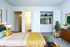 Inviting bedroom with elegant decor, featuring a cozy bed with vibrant pillows, a modern open closet with colorful attire, and stylish furniture accented with fresh greenery.
