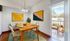 Bright and inviting dining area with modern decor, featuring a wooden table set for four, vibrant abstract artwork, and a petite balcony view.