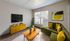 Bright and stylish living room with a green sectional sofa, vibrant yellow accents, and modern decor, bathed in natural light from a large window.