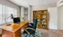 Bright and inviting home office space with a sleek wooden desk, modern lamp, and comfortable green chair, ideal for productivity. Large window provides natural light, with a stylish bookshelf enhancing the cozy atmosphere.