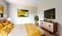 Inviting bedroom with vibrant yellow accents, chic decor, wall-mounted TV, and a modern dresser, designed for cozy relaxation.