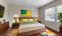 Bright and cozy bedroom featuring a modern wooden bed with vibrant pillows, large windows with natural light, and stylish decor.