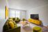Chic living room with vibrant green sofa, stylish yellow accents, and a sleek modern coffee table under natural light from a large window.