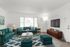 Bright and inviting living room featuring teal sofas and ottomans, a stylish coffee table with pink flowers, and large windows for ample natural light.