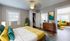 Charming bedroom with modern decor, vibrant teal and yellow accents, leading to a stylish living area with a bright yellow sofa.