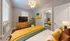 Charming bedroom with vibrant decor, featuring a cozy bed, chic wooden dresser, and modern artwork, bathed in natural light.