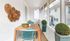 Charming sunlit porch with a stylish wooden dining table, cozy turquoise chairs, and vibrant potted plants, perfect for relaxing dining.