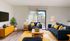 Modern living room with stylish navy sofas, vibrant yellow accents, and abundant natural light, enhanced by a large sliding glass door leading to a scenic view. Elegant decor includes a sleek TV, contemporary lamps, and a lush indoor plant.