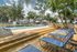 Inviting outdoor pool area with sun loungers, surrounded by lush greenery and contemporary apartment buildings, perfect for relaxation.