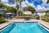 Charming apartment complex featuring a refreshing outdoor pool, relaxing patio furniture, and a barbecue area surrounded by lush greenery and elegant architecture.
