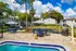Inviting community pool area with elegant patio seating surrounded by lush greenery and modern apartment buildings under a vibrant blue sky.