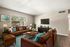 Inviting living room with elegant brown leather sofas, vibrant teal accents, large window view, and modern entertainment center.