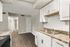 Charming modern kitchen with elegant granite countertops, white cabinetry, and sleek wood flooring leading to a cozy hallway.