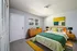 Bright modern bedroom featuring a cozy double bed with green and yellow accents, elegant wooden furniture, and vibrant wall art.