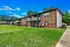 Charming brick apartment complex with spacious balconies, nestled in a serene green landscape under a clear blue sky.